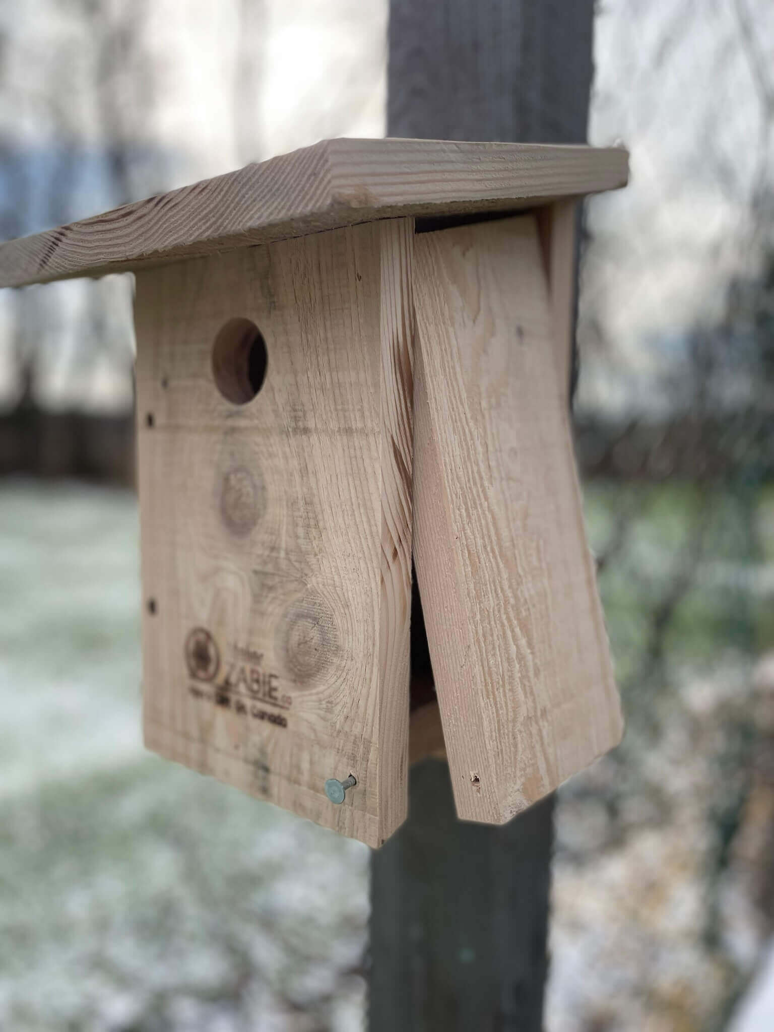Une maison pour oiseaux fixée à un poteau, entourée de neige.