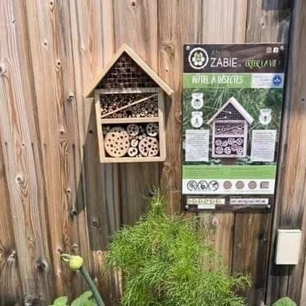 Maison à abeilles avec un panneau et une plante à proximité, située dans un emplacement naturel.
