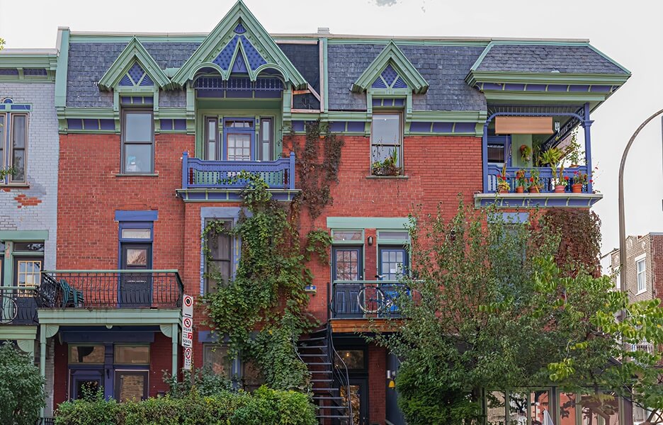 Façade d'une maison en briques rouges avec des plantes grimpantes et des balcons colorés.