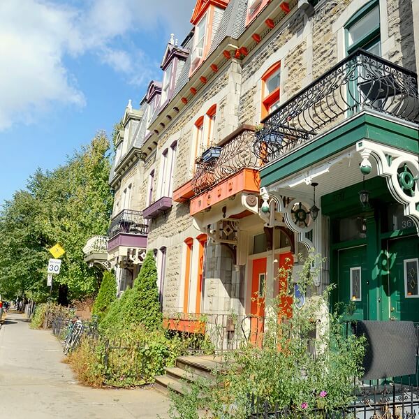 Une rue résidentielle de Montréal avec des maisons en pierre grise, des portes colorées en vert et orange et des balcons en fer forgé.